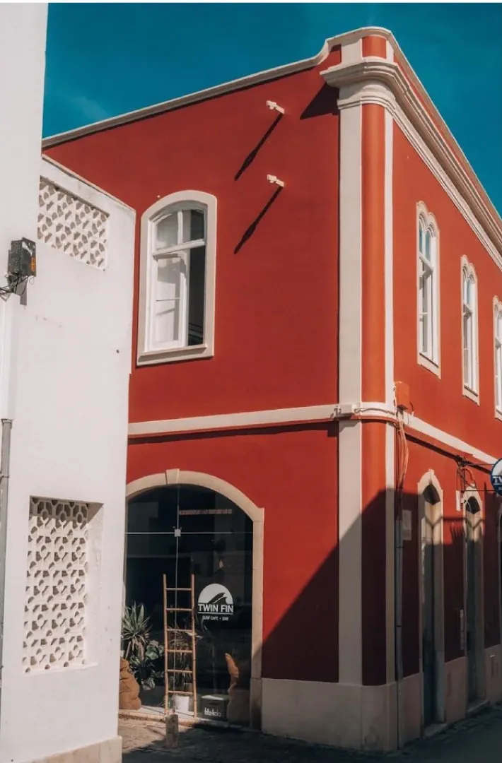 Twin Fin’s red corner building on Rua Gil Vicente, with an arched glass door