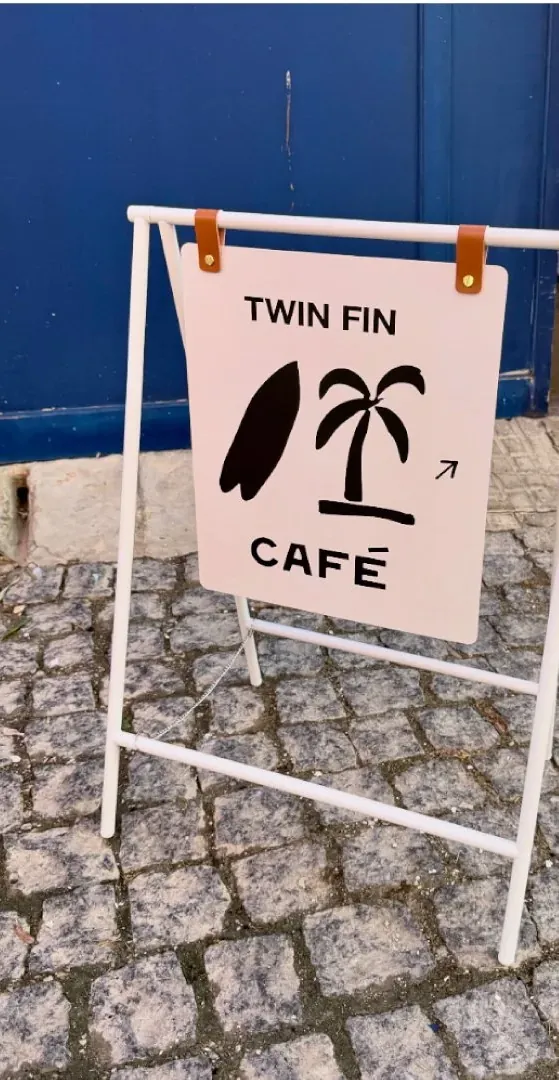 The Twin Fin cafe sign on the cobbled street, with a surfboard and palm tree